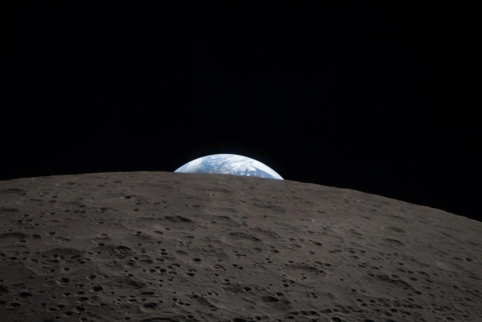 The blue and white Earth, partly in shadow, sinking behind the grey, cratered edge of the Moon, seen from the Orion spacecraft