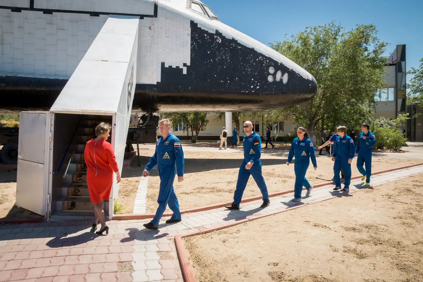 Astronauts in blue flight suits walk past a Buran orbiter on display outside a museum building