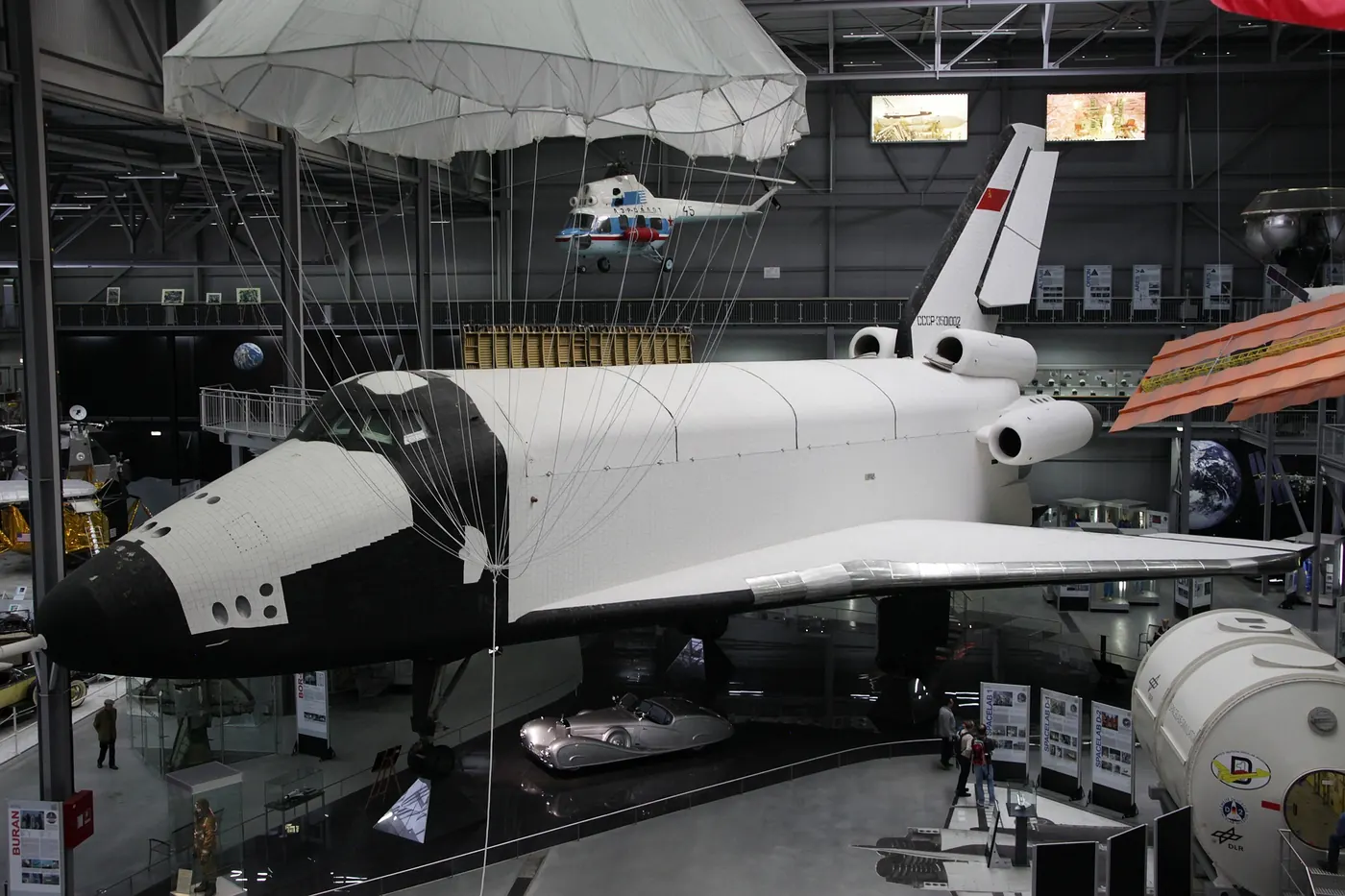 A full-size white Buran test orbiter with black heat tiles, on display inside a museum hall