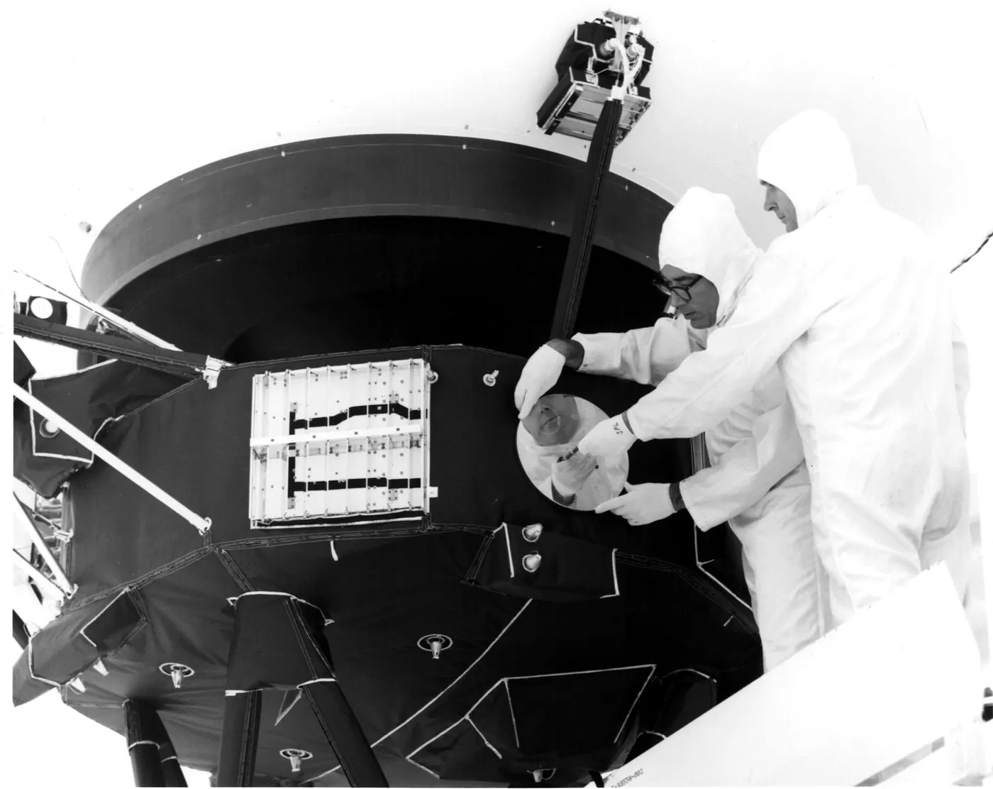Engineers in clean-room suits attach a cover over the gold record on the side of the Voyager 1 spacecraft