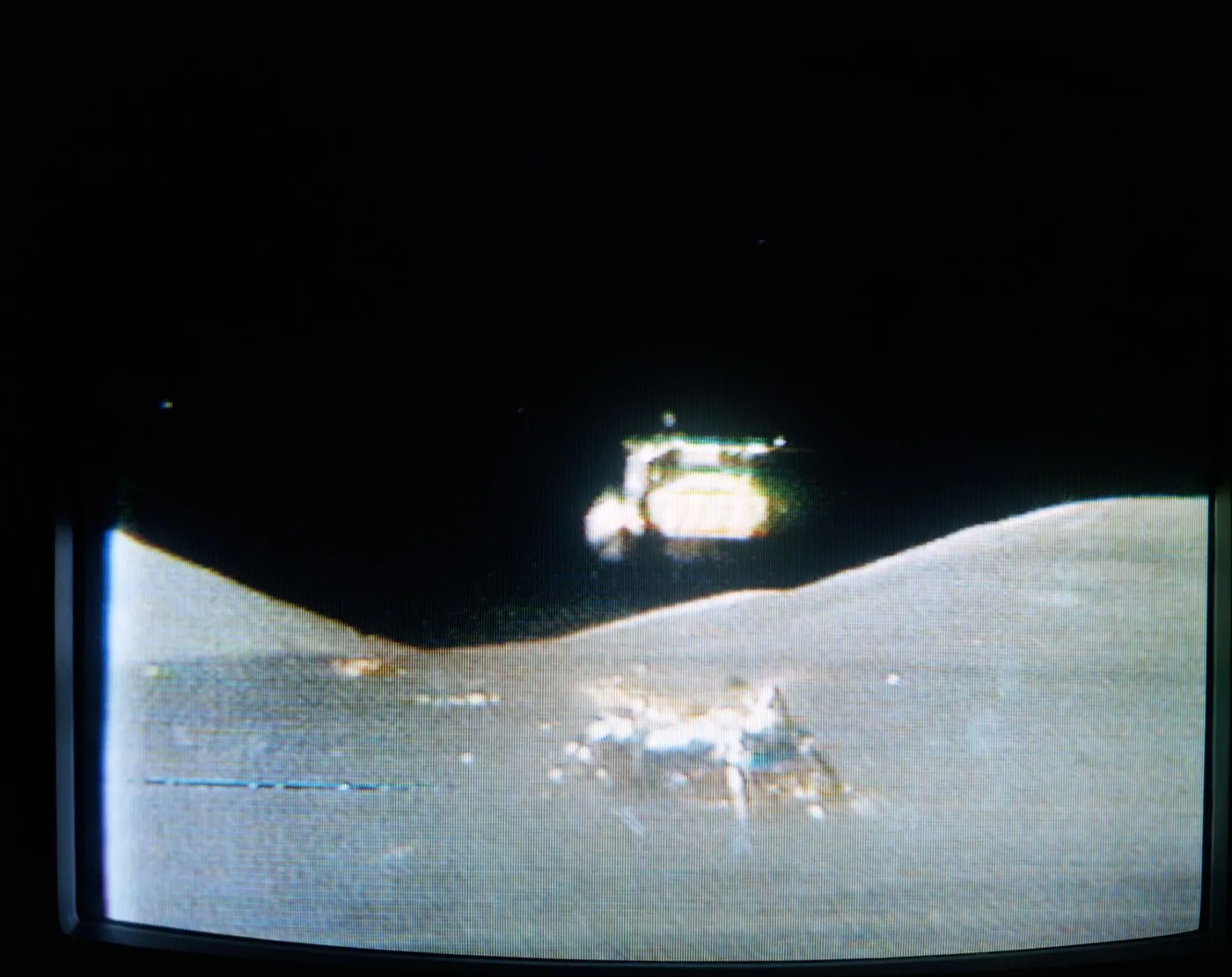 Grainy colour television image of the Apollo 17 lunar module ascent stage rising above the grey lunar surface